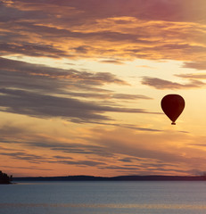 Hot air balloon flying over lake at sunset