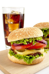 Set of two cheeseburgers and glass of cola on wooden board