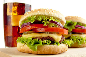 Macro view of cheeseburgers and glass of cola on wooden board