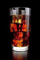 Glass of cola with ice cubes on black wooden table