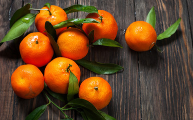 Fototapeta na wymiar Clementine mandarines with leaves on dark wooden background