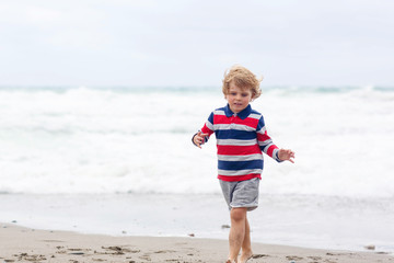 Fototapeta na wymiar Little kid boy playing on beach on stormy day