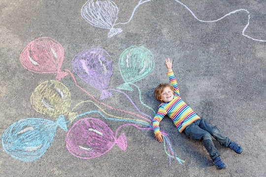 Kid boy having fun with colorful balloons drawing with chalks