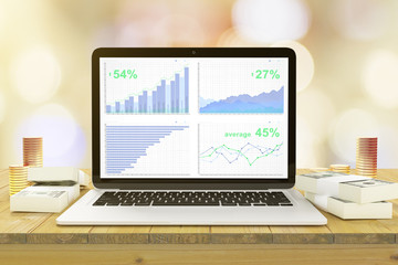 Financial charts on laptop screen on a wooden table with a stack