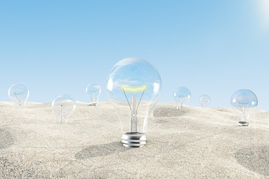 Glowing light bulb among others in the sandy desert with blue sk