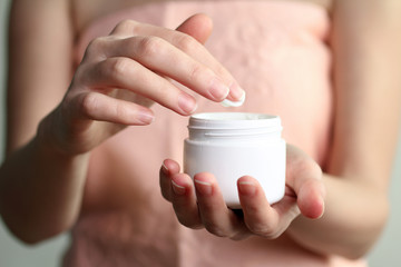 Woman dipping finger into moisturizer cream on white isolated background