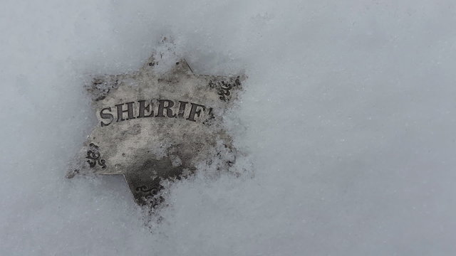 Snow falling on sheriff badge.