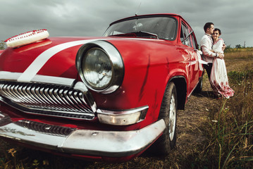 Obraz na płótnie Canvas stylish bride and happy groom near red retro car on the backgrou