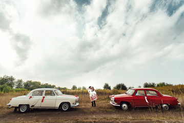 Obraz na płótnie Canvas stylish bride and happy groom near two retro cars on the backgr