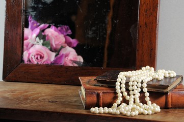 Fototapeta na wymiar String of pearls, books and antique mirror. Focus on pearls.
