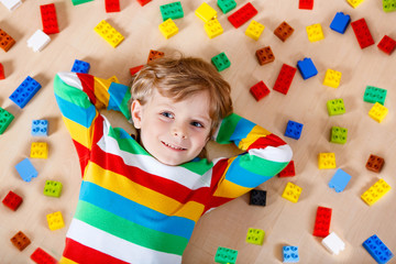Little blond child playing with lots of colorful plastic blocks