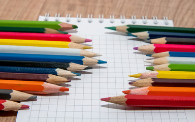 Set of colorful pencils lying in row on white paper sheet