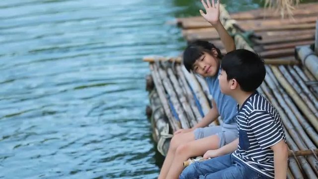 Young Asian brother and sister playing water in bamboo raft