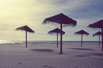 Wooden sun umbrellas silhouettes on the sea beach. Vacation concept in vintage color tone. Costa Dorada, Spain