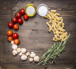 Fototapeta na wymiar Ingredients for cooking vegetarian raw fusilli pasta with sunflower oil cherry tomatoes, mushrooms, rosemary place for text,frame on wooden rustic background top view