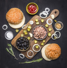 Food burger with tuna Food burger with tuna, herbs, cucumbers, olives, onions and sauce on a cutting board on wooden rustic background top view 
