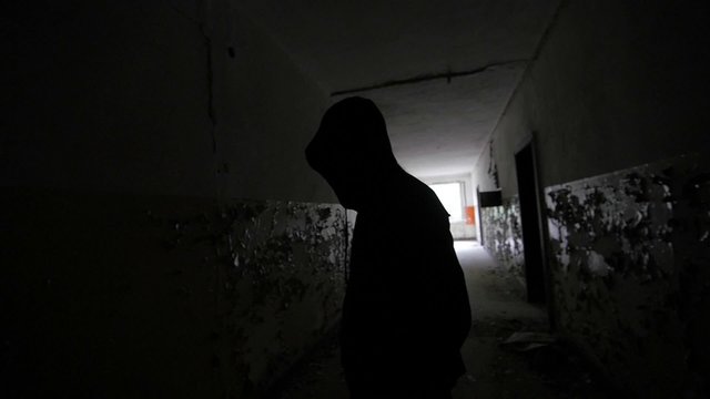 Slow motion of a scary guy with hood in an abandoned building backlight