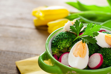 Salad with broccoli, eggs and radishes in a small bowl on wooden background and tulip bouquet, with copy space.