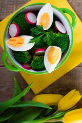 Salad with broccoli, eggs and radishes in a small bowl on wooden background and tulip bouquet.