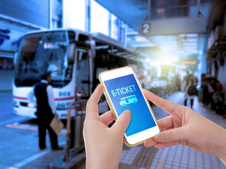Hand holding mobile phone with E-Ticket word with blur bus termi