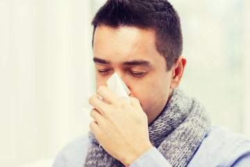 close up of ill man with flu blowing nose at home