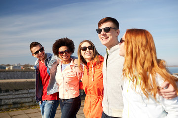 happy teenage friends walking along city street