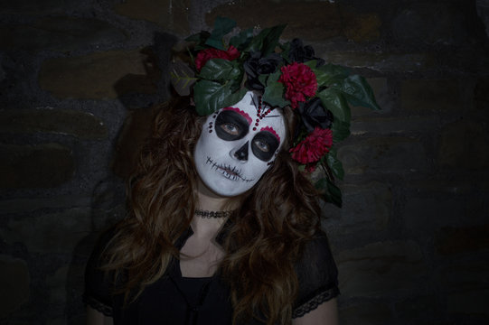 Portrait image of an attractive young woman dressed in a Mexican day of the dead inspired costume. taken with a brick wall background