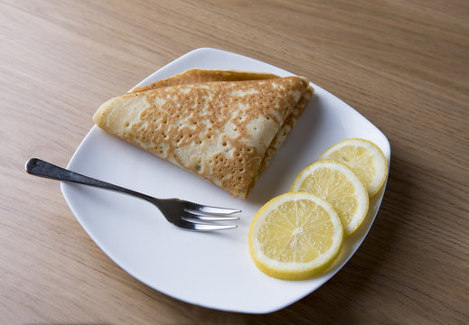 Image of a pancake on a white plate with three slices of lemon and a fork 