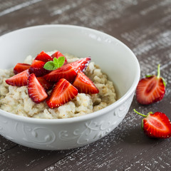 Oatmeal with honey and strawberries in a white bowl on a dark wooden table. Healthy breakfast