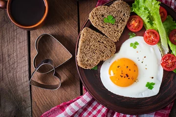 Wall murals Fried eggs Breakfast on Valentine's Day - fried eggs and bread in the shape of a heart and fresh vegetables. Top view