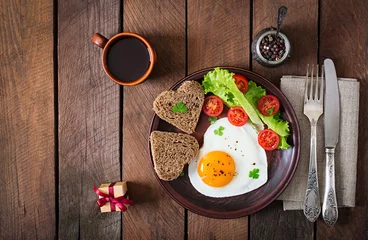 Poster Oeufs sur le plat Petit-déjeuner le jour de la Saint-Valentin - œufs au plat et pain en forme de cœur et légumes frais. Vue de dessus