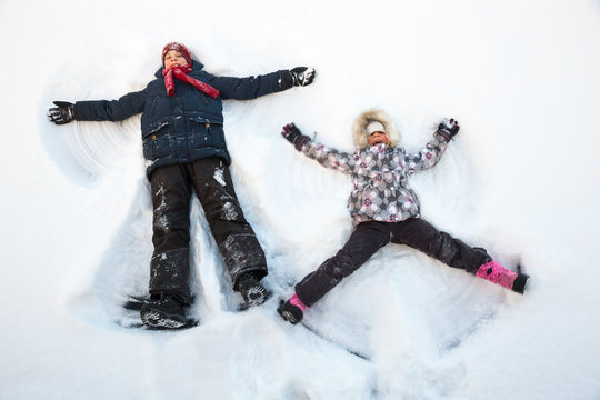 Happy boy and girl having fun together lying in a snow making snow angels