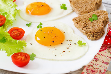 Breakfast on Valentine's Day - fried eggs and bread in the shape of a heart and fresh vegetables.