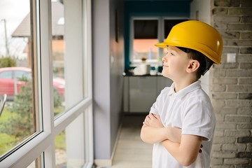 Little boy wearing a engineering helmet and looking throught windows