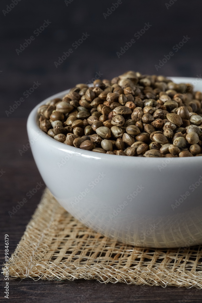 Wall mural A white ceramic bowl full of hemp seeds, close up