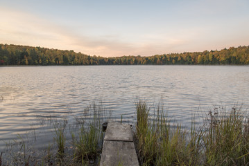 A lake with a surrounding forest in fall colors in Wisconsin.  A small wooded dock extends from the shore.