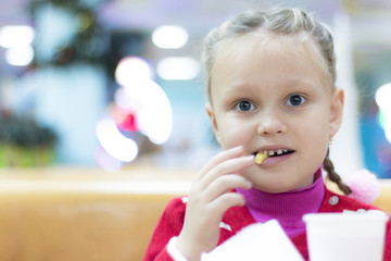 Beautiful laughing little girl sitting at table and eating French fries.