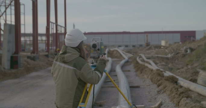 Girl with Land Surveyor Total Station on the Background of Construction.