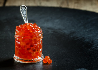 Red caviar in a glass jar on black stone background, selective f