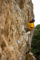 Young male climber hanging by a cliff.