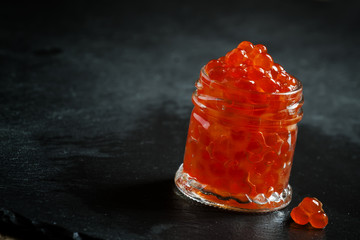 Red caviar in a glass jar on black stone background, selective f