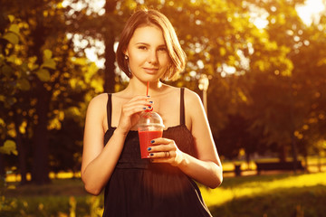 Beautiful young girl is drinking fresh smoothies on a sunny day. Healthy food. Useful vitamin cocktails. Stylish hipster woman on a red background