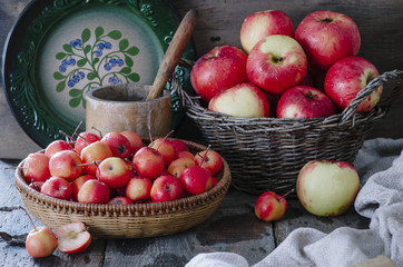 Rustic baskets with small and big red apples, wooden mortar and green plate on wooden background