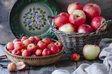 Old baskets with red apples and green plate on wooden background