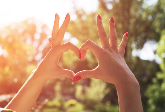 Woman's hand make a heart during beautiful spring sunset