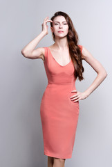 Portrait of a young attractive woman with beautiful long brown hair. She wears a coral dress and small earrings. She touches her head in an elegant gesture.