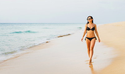 Fototapeta na wymiar Vacation on the sea. Young sexy caucasian woman walk on ocean beach. 