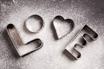 Love shaped cookie cutters and flour on black background