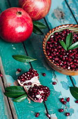 Миска гранатовых зерен и целые гранаты на старом деревянном фоне.