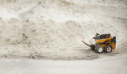 Yellow snow removing bulldozer near big snow piles